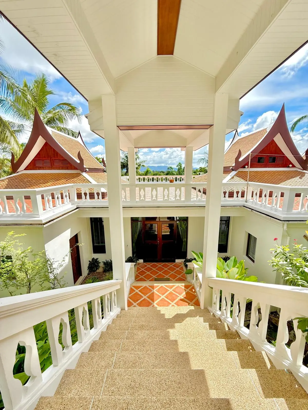 Covered walkway between Thai-style villa pavilions with terracotta-tile roofs