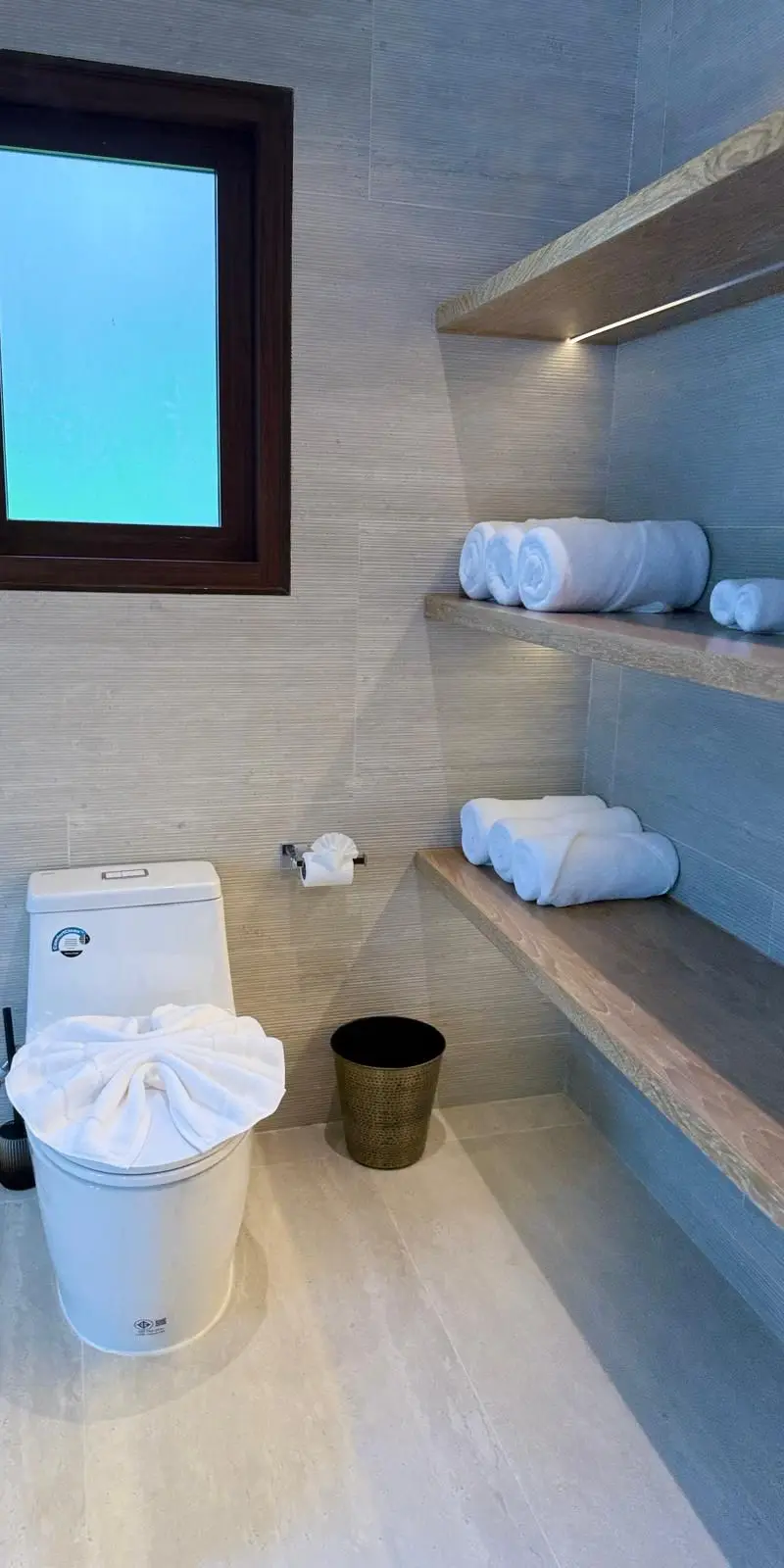 Powder room with neatly folded towel rolls on floating wooden shelves