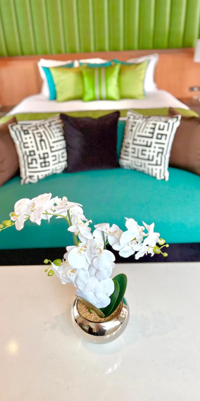Guest bedroom with green channel-tufted headboard and teal velvet love-seat