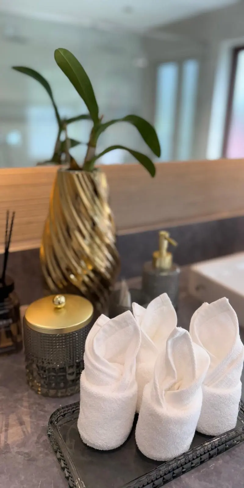 Bathroom vanity styling — orchid, gold accents, rolled white towels