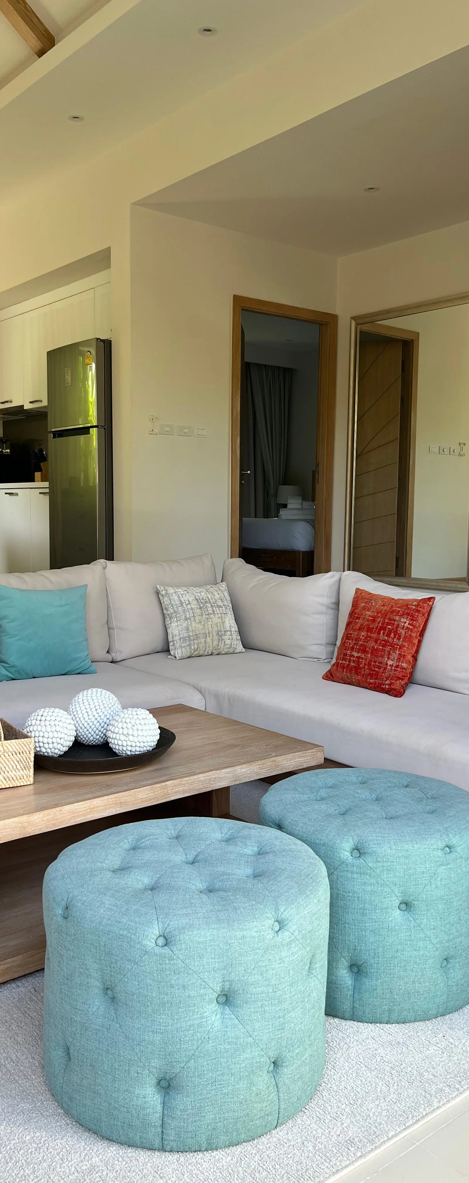 Living room with beige sectional, teal accent cushions and open kitchen beyond
